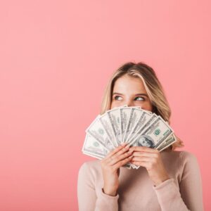 Photo of woman peeking over fanned-out dollar bills.