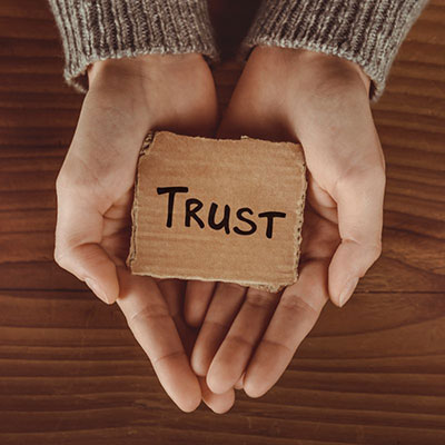 Photo of two hands together cradling a small, printed sign that reads, "Trust"