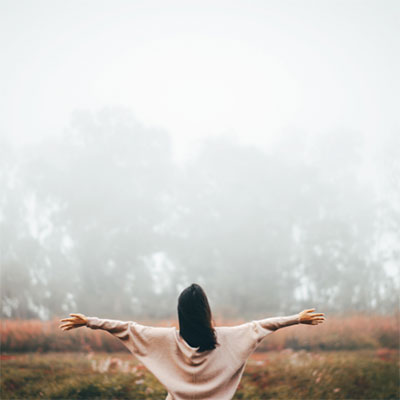 photo of woman, standing outside on a foggy day, with her back to the camera, arms outstretched