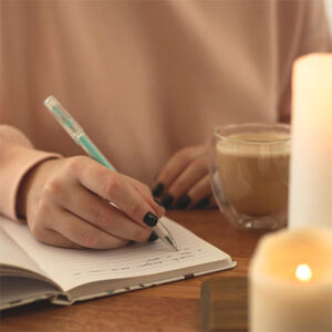 Close up of woman sitting at desk, writing in journal.